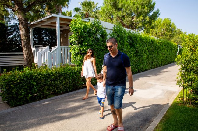 Due adulti e un bambino camminano su un vialetto, circondati da alberi e siepi.
