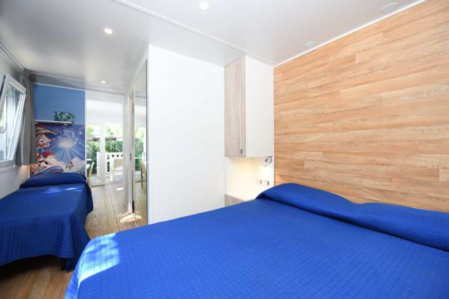 Una camera con letto matrimoniale e singolo, copriletti blu e parete in legno.