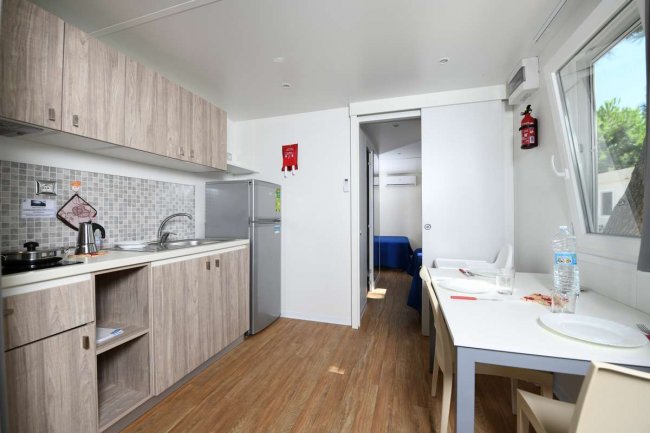 Interno di una cucina moderna con mobili in legno chiaro, tavolo da pranzo e grande finestra.