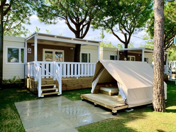 Bungalow in legno con veranda bianca e piccola tenda accanto su prato.
