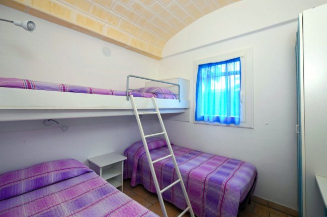 Camera con due letti singoli e un letto a castello, copriletti colorati e finestra blu.