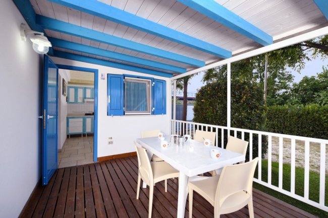 Terrazza coperta con tavolo bianco, quattro sedie e vista sul giardino.