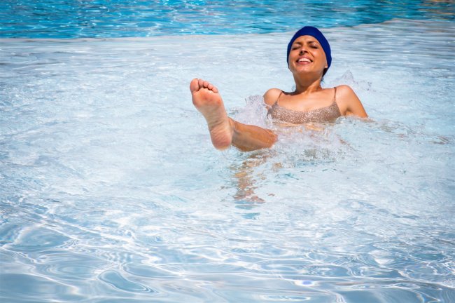 Persona in piscina con cuffia blu e sorriso mentre gioca nell'acqua.