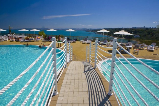 Piscina con passerella e ombrelloni vista mare.