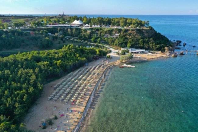 Una spiaggia con ombrelloni e lettini vicino a una collina verde.