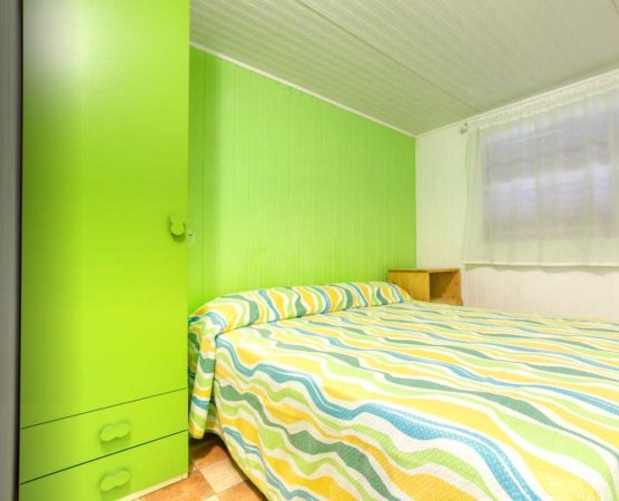 Una camera da letto con pareti verdi, un armadio e un letto con copriletto a righe colorate.