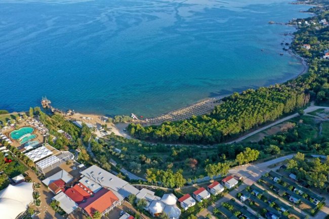 Vista aerea di un resort con piscina, spiaggia e mare turchese circondato da vegetazione.