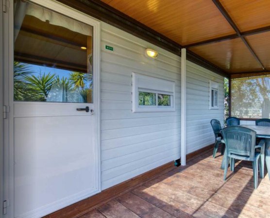 Veranda coperta con tavolo e sedie verdi accanto a casa mobile bianca.
