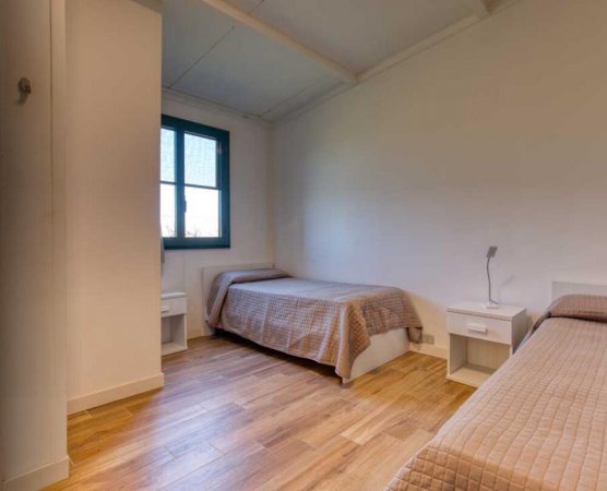 Due letti singoli con copriletti beige, pavimento in legno e una finestra con cornice verde.