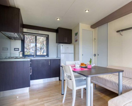 Cucina moderna con mobili scuri, tavolo apparecchiato e divano beige vicino a una finestra.