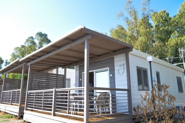 Una casa mobile con ampio portico e sedie, circondata da alberi.