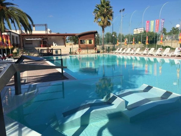Piscina all'aperto con lettini e vegetazione circostante.