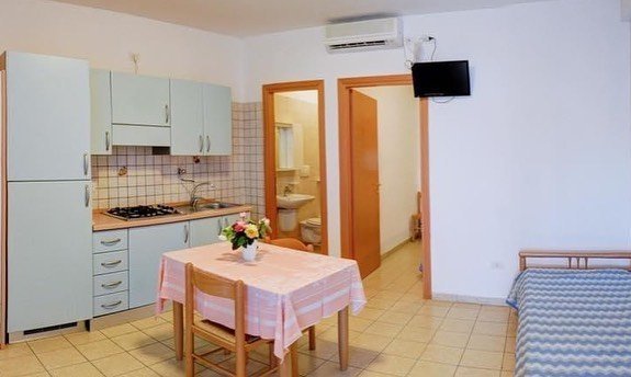 Monolocale con cucina, tavolo, letto e porta aperta sul bagno.