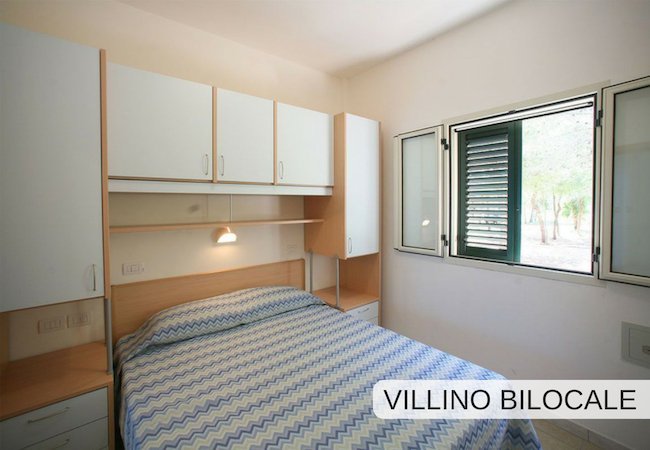 Una camera da letto con letto matrimoniale, mobili bianchi e una finestra aperta.