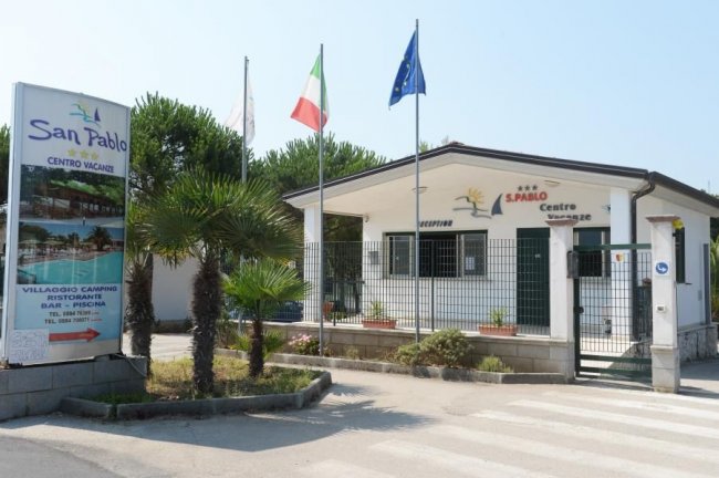Ingresso di un centro vacanze con cartello e bandiere.