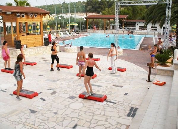 Donne partecipano a una lezione di fitness su pedane vicino alla piscina.