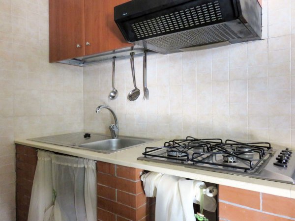 Cucina con piano cottura, lavello e utensili pendenti, rifinita con mattoni e piastrelle.