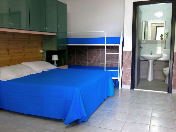 Camera con letto matrimoniale e letti a castello. Bagno visibile sullo sfondo.