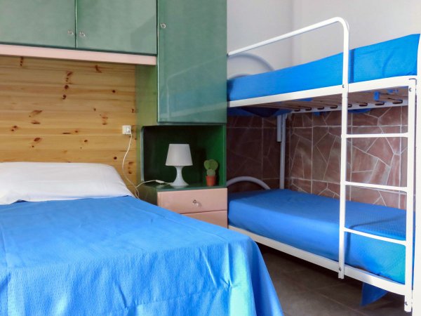 Camera con letto singolo e letto a castello, copriletti blu e mobili verdi.