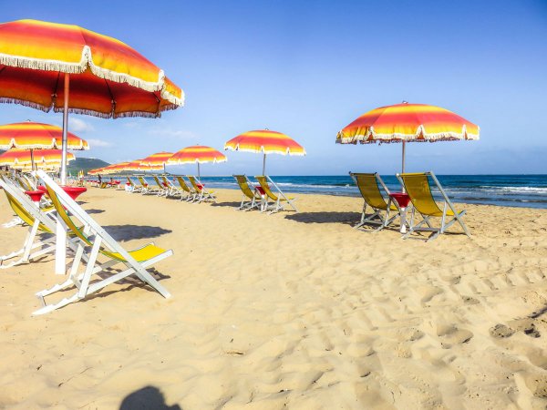 Spiaggia con ombrelloni arancioni e gialli e sedie a sdraio in fila.