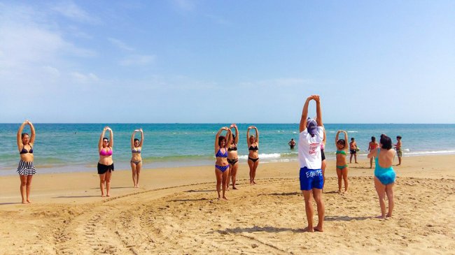 Persone fanno esercizi sulla spiaggia, rivolte verso il mare.