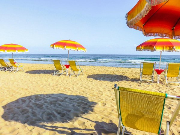 Ombrelloni colorati sulla spiaggia, con sdraio di fronte al mare.