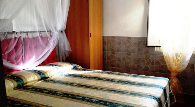 Camera da letto con letto matrimoniale, zanzariera, armadio in legno e tendaggi chiari.