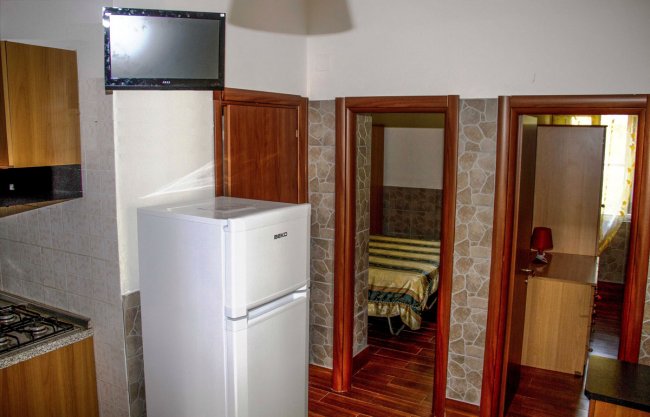Interno con frigorifero, TV a muro e porte che conducono alle camere.