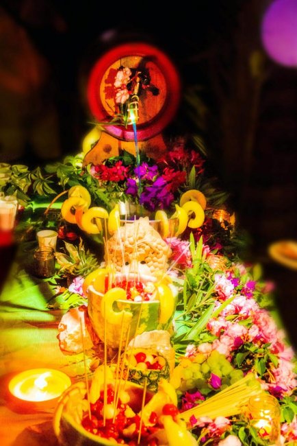 Tavolo decorato con frutta, fiori e luci soffuse, creando un'atmosfera vivace e festosa.