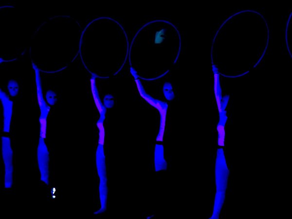 Figure con tute fluorescenti e cerchi illuminati in un ambiente scuro.