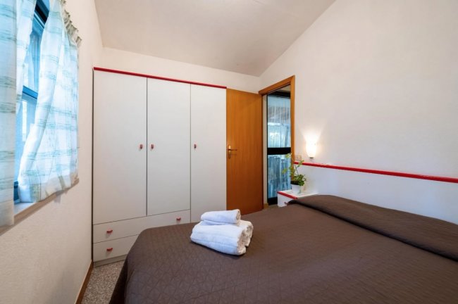 Camera da letto con letto matrimoniale, armadio bianco e finestra con tendine.