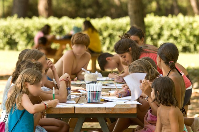 Bambini seduti a un tavolo all'aperto, impegnati in attività artistiche con pennarelli colorati.