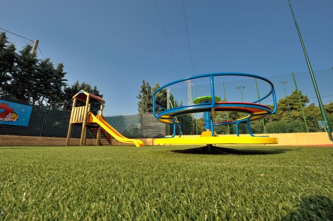 Parco giochi con scivolo giallo e giostra circolare colorata su prato artificiale.