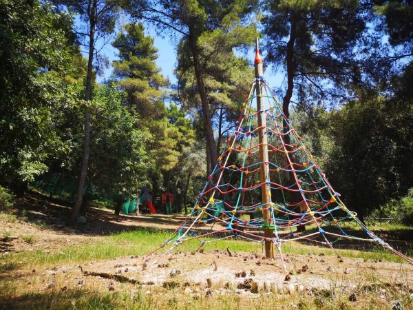 Una piramide di corde colorate in un'area giochi all'aperto circondata da alberi.