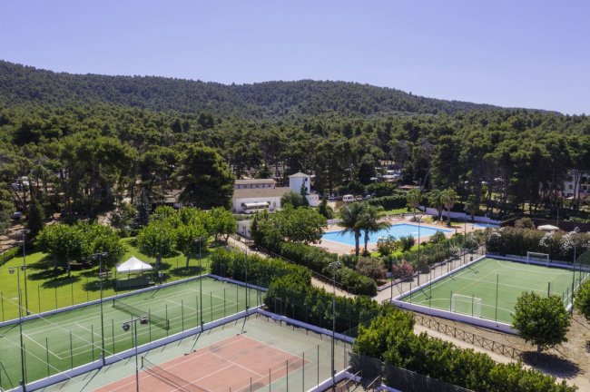 Complesso sportivo con campi da tennis, piscina e alberi circostanti.