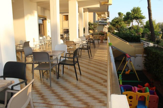Terrazza con tavoli e sedie, vista sul giardino con area giochi bimbi.