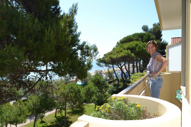 Donna sul balcone con vista su alberi e mare.