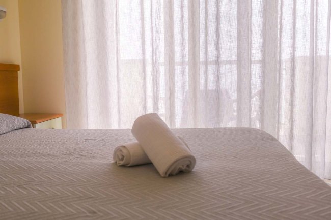 Letto matrimoniale con lenzuola grigie e due asciugamani bianchi arrotolati.