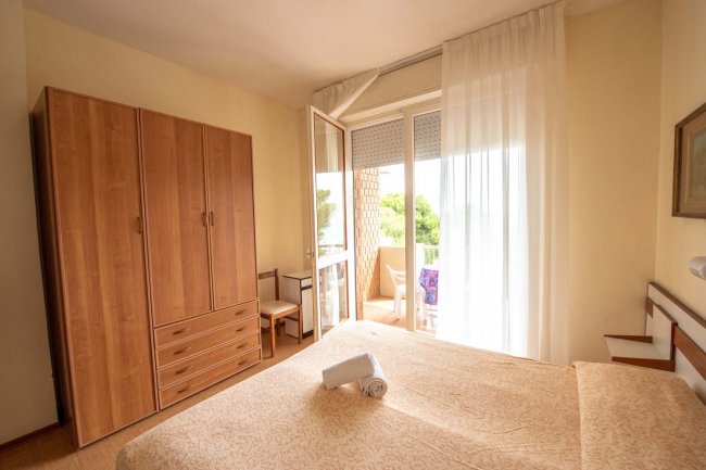 Una camera da letto con armadio in legno, letto matrimoniale e porta finestra aperta su un balcone.