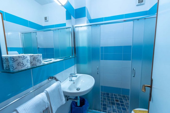 Un bagno moderno con doccia, lavabo, specchio ampio e piastrelle blu e bianche.