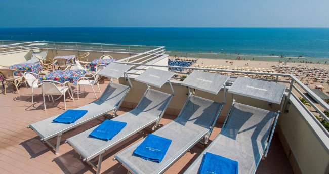 Terrazza con lettini e vista sul mare e spiaggia affollata.