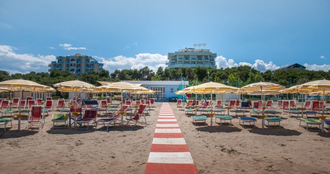 Spiaggia con ombrelloni gialli e lettini, accesso centrale con passerella rossa e bianca.