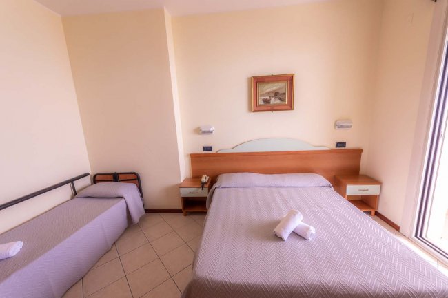 Camera da letto con letto matrimoniale e singolo, pareti chiare.