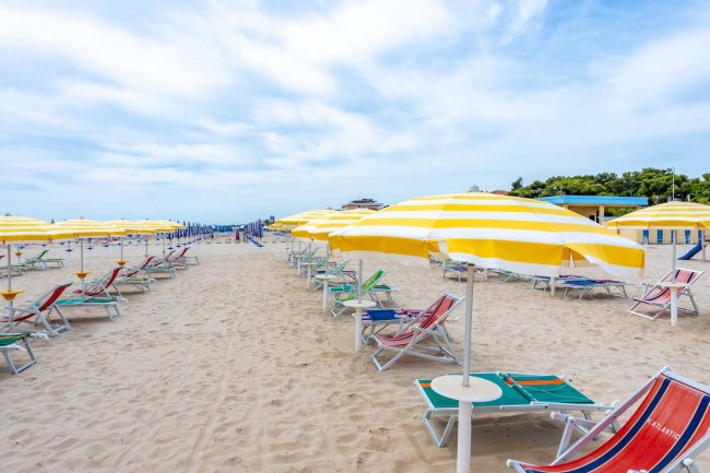 Spiaggia con file di ombrelloni gialli a righe e sedie a sdraio.
