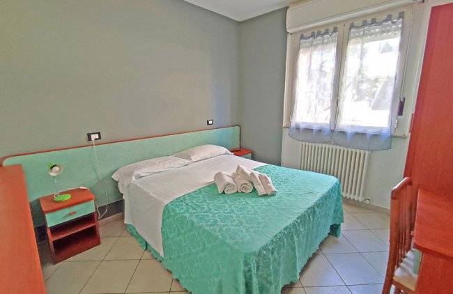 Stanza con letto matrimoniale, copriletto azzurro, finestra con tenda, e mobili coordinati.