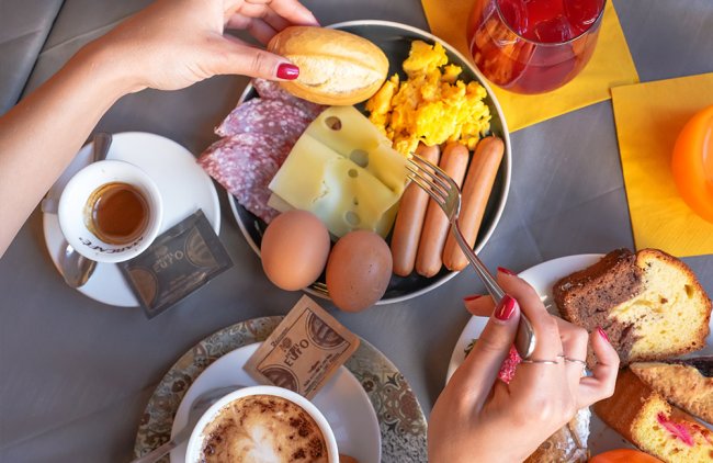 Colazione con uova, salumi, formaggio, caffè, succo e dolci.