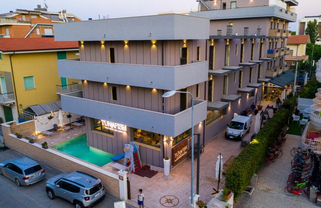 Hotel moderno con piscina e auto parcheggiate davanti.