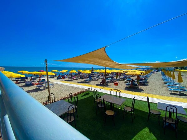 Spiaggia con ombrelloni gialli e tavoli sotto copertura.