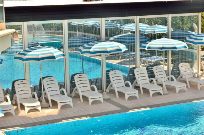 Lettini bianchi e ombrelloni a strisce blu e bianche accanto a una piscina.
