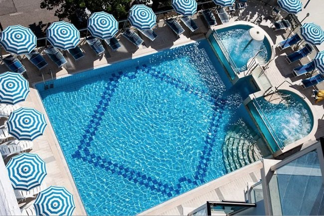 Vista dall'alto di una piscina con ombrelloni a righe blu e bianche disposti intorno.